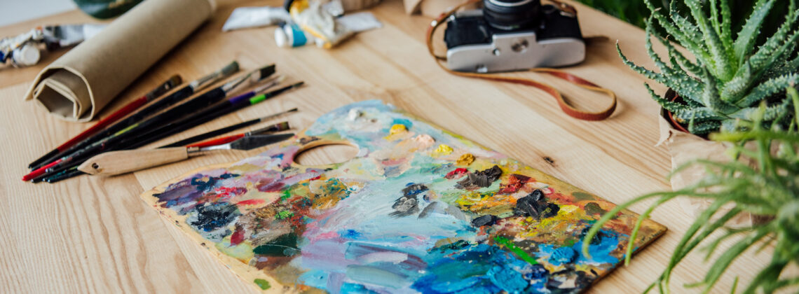 Creative workplace with art supplies, vintage camera and potted succulent plants