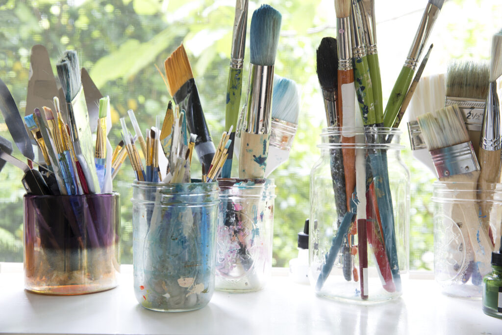 Row of jars with variety of artist paintbrushes on window sill  of artists studio